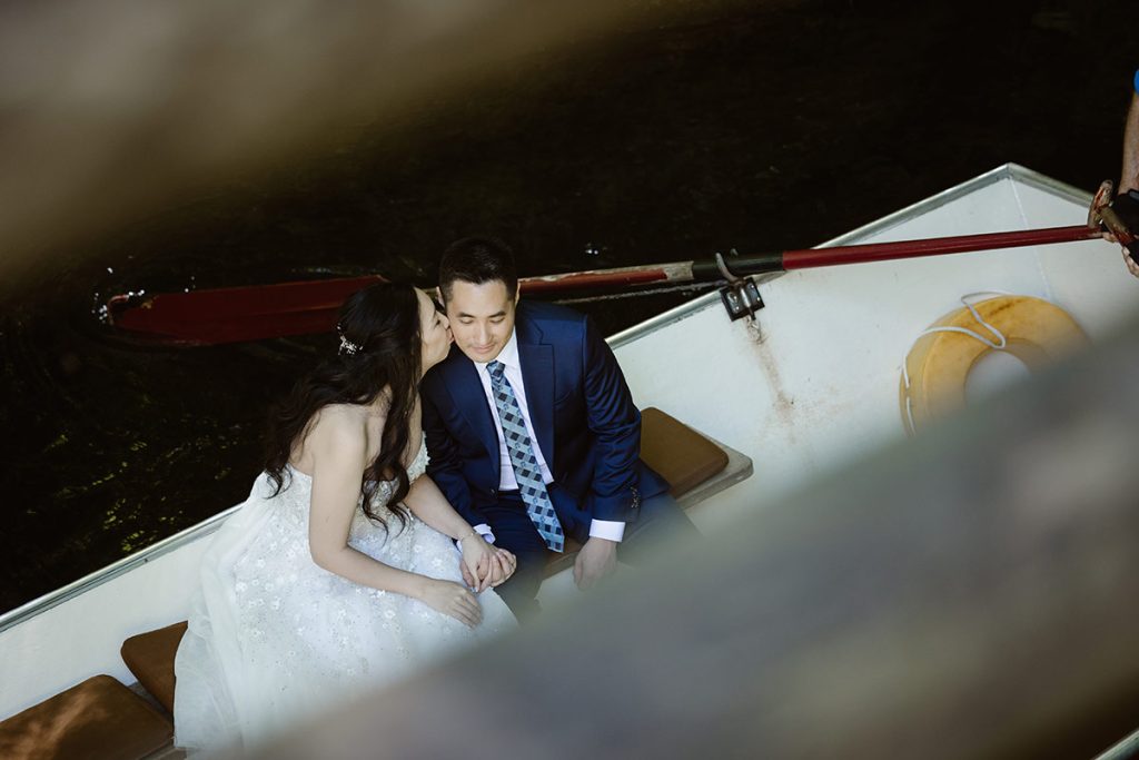 A bride and groom sit in a rowing boat on their wedding day in the Jungfrau Region, Switzerland