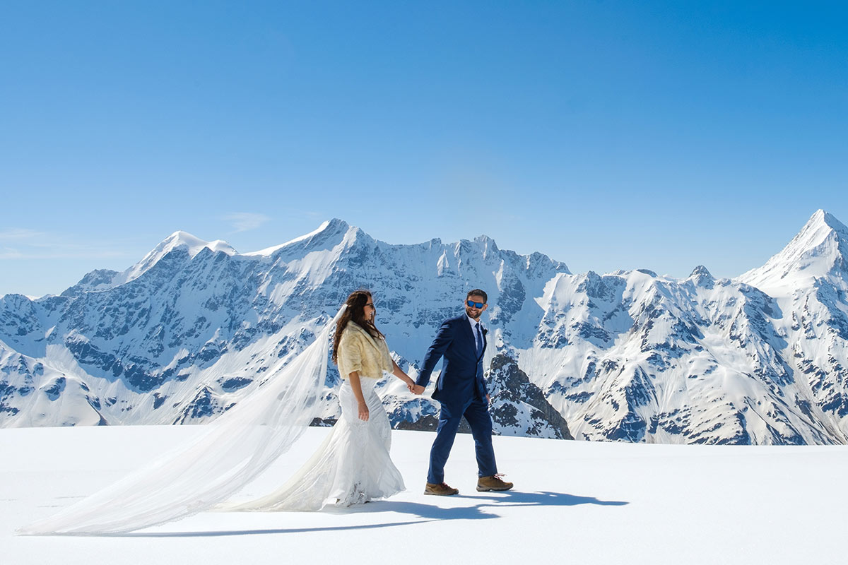 A bride and groom walk hand in hand across the Glacier above Lauterbrunen and Wengen, Switzerland, getting wedding photographs taken on their elopement wedding ceremony